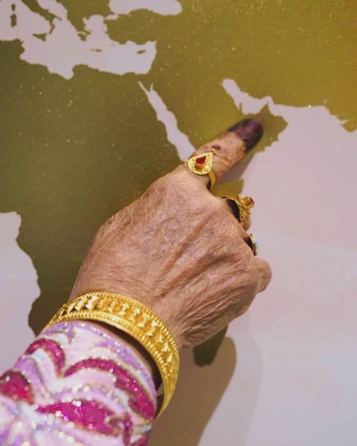 A hand wearing gold bangles and rings pointing to the Gulf on a gold world map.